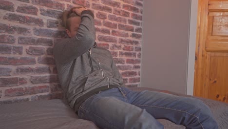 young man casually sits down on the bed, rubs his hair, and starts using his laptop after showing that he has had an exhausting day