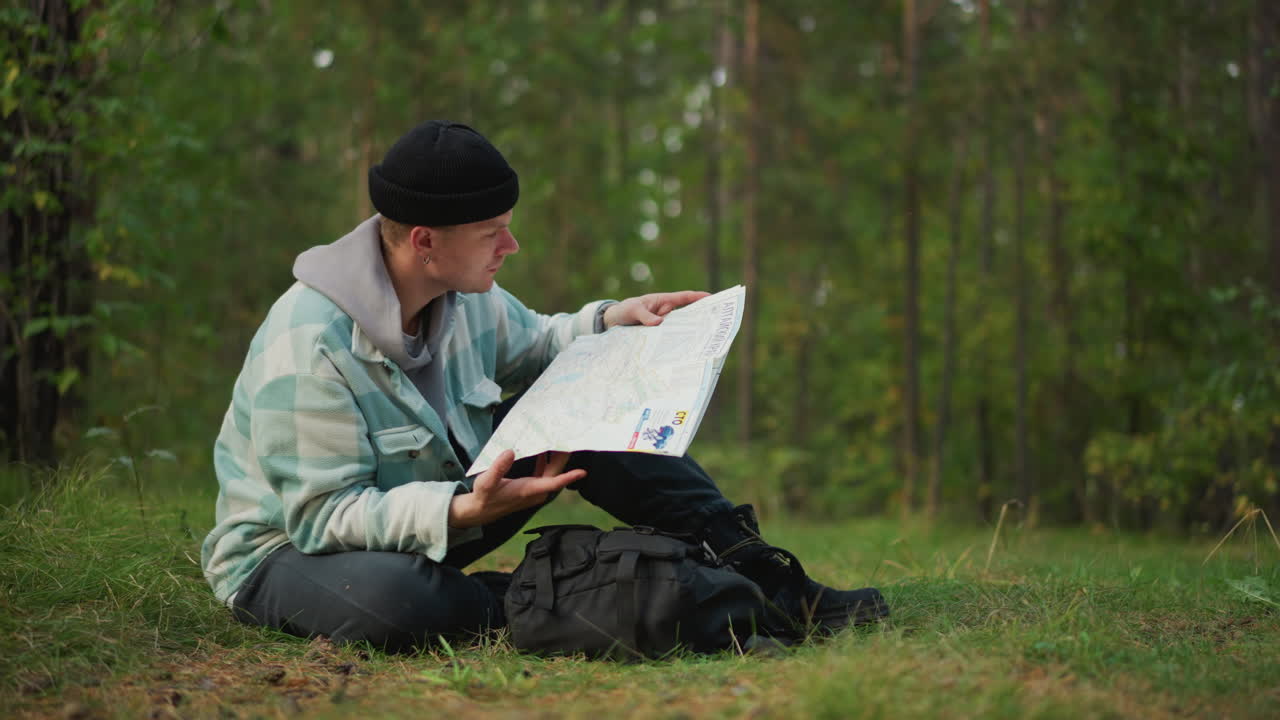 white hiker in forest studying map, sits beside backpack scanning route, pauses to check compass, rummages through gear, contemplates path ahead, soft daylight, pine trees, quiet solitude
