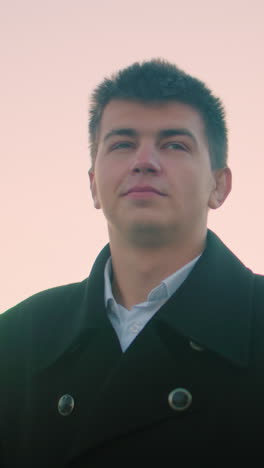 business man black suit outdoor at dusk drinking coffee with confident expression, background features modern building, parked cars, and structures