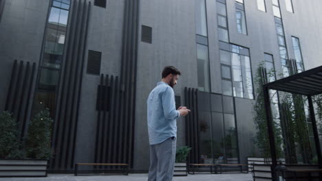 hombre de negocios enviando mensajes de texto de pie en un moderno edificio de oficinas de vidrio. usuario de la aplicación enfocado