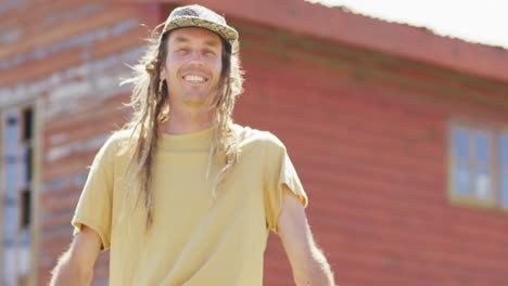 video portrait of smiling caucasian male artist with dreadlocks sitting on wall in the sun