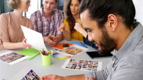 hombre sosteniendo fotos mientras los ejecutivos de negocios usan portátil en la reunión