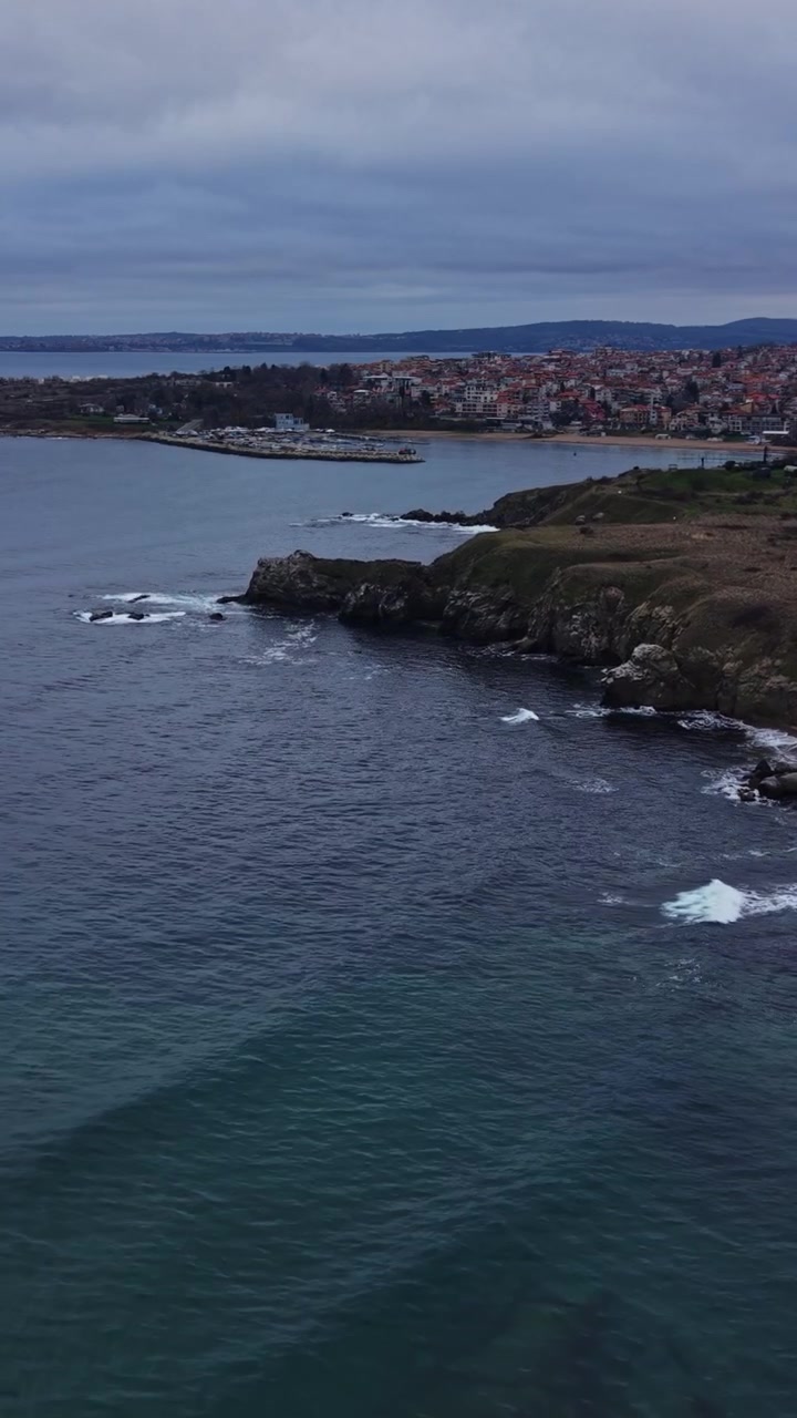 Vista della costa con onde e scogliere vicino a una città al tramonto