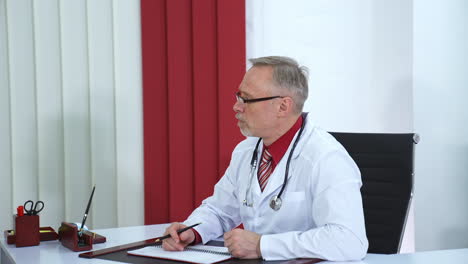 male doctor speaks with patient in office. selective focus on senior male medic at table in scrubs and phonendoscope on neck. phisician at work.