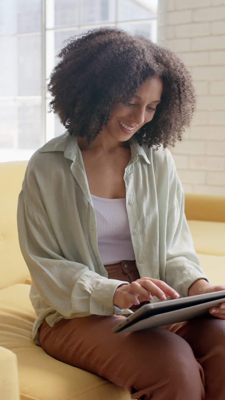 Vertical video of portrait of happy biracial businesswoman using tablet in office