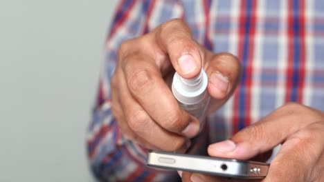 hombre desinfectando su teléfono inteligente con spray de desinfectante de manos