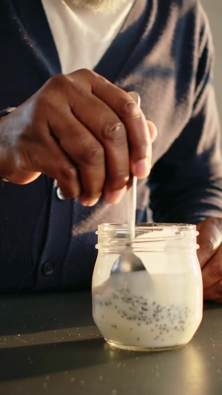 Video verticale: Uomo con cardigan blu scuro che posiziona un cucchiaio e mescola la chia in un barattolo in cucina per colazione.