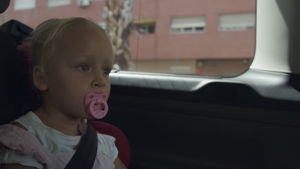 Toddler girl with pacifier traveling by car Safe ride in child seat