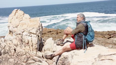 Happy-senior-biracial-man-in-mountains-resting-at-sea,-in-slow-motion