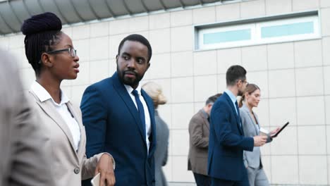 caucasian couple of african american businessman and businesswoman walking down the street in the morning, talking and using smartphone