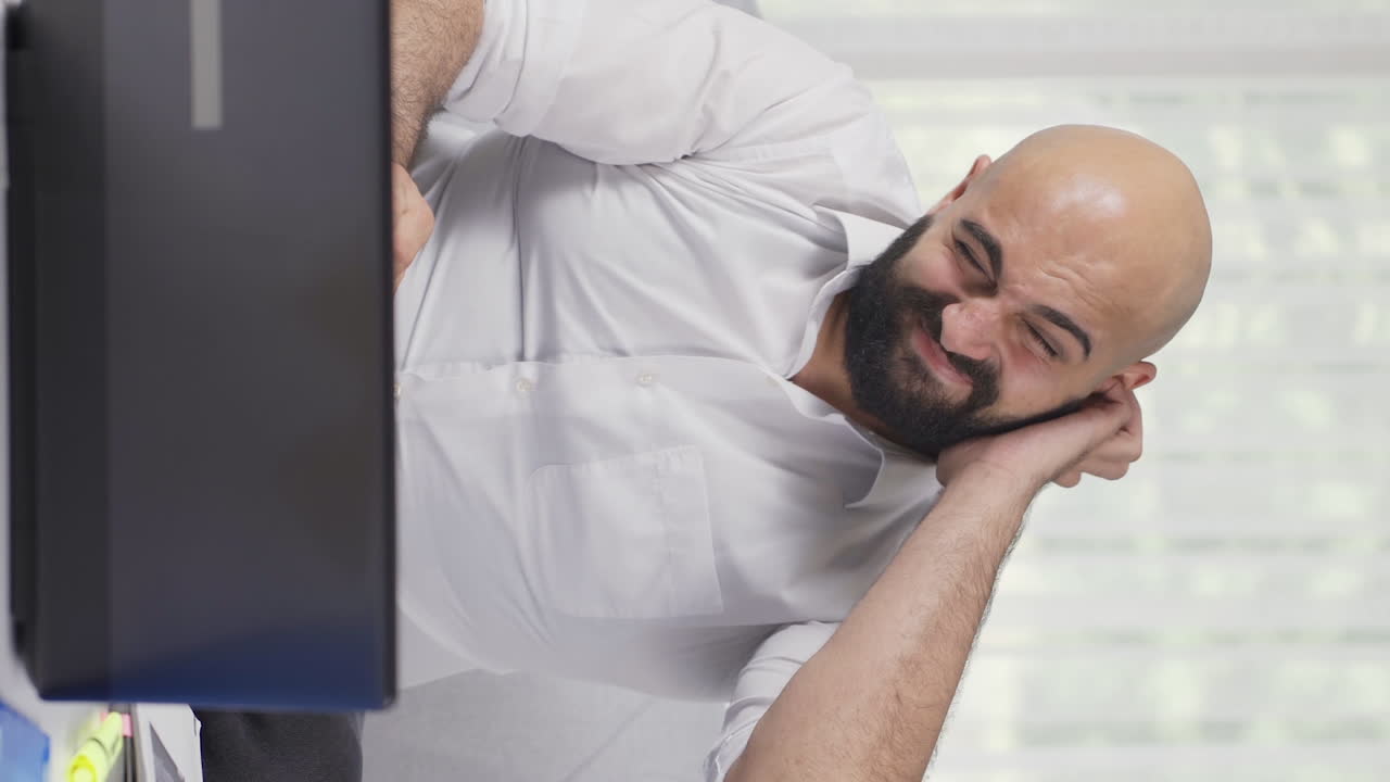 Vertical video of Home office worker man scratches his ears looking at camera.