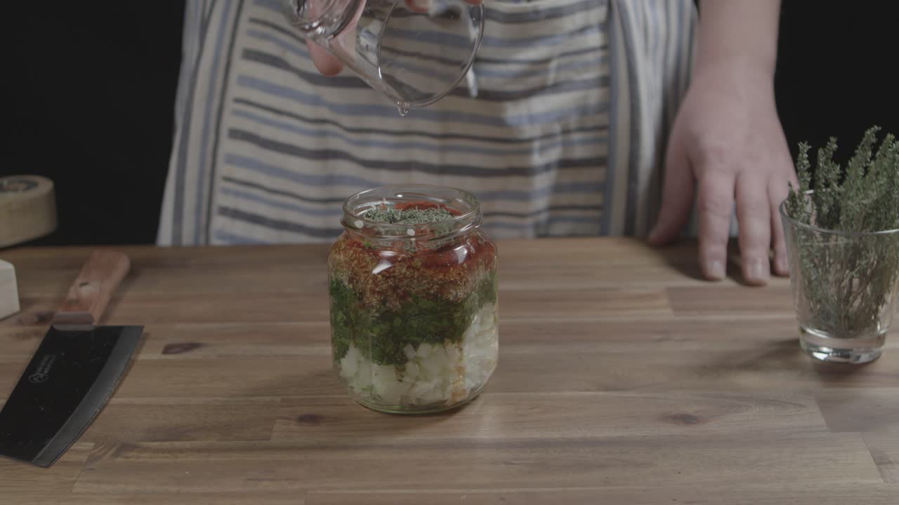 바베큐 를 위한 아르헨티나 치미추리 소스 를 준비 하기 위해 재료 들 을 담은 유리 용기 에 기름 을 넣는다