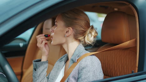 woman applying red lipstick in car