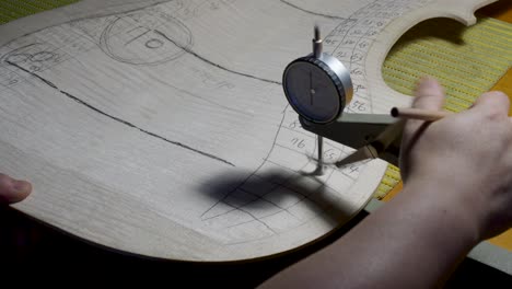 fabricante de instrumentos de cuerda maestro luthier proceder con el trabajo de graduación en la placa trasera del violonchelo, usar calibre medidor de grosor, medir niveles, usar lápiz escribir valores en madera, taller de cremona, italia