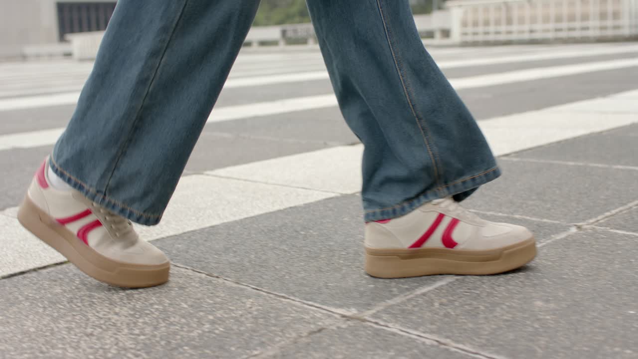 Person entering from left and walking across stone-tiled plaza in jeans with white canvas sneakers