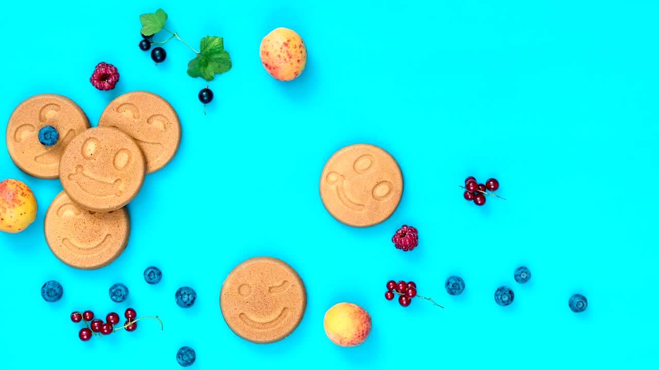 detener el fondo de la comida en movimiento. deliciosos panqueques de mini sonrisa con bayas en superficie azul, vista de arriba, escena dinámica, video 4k