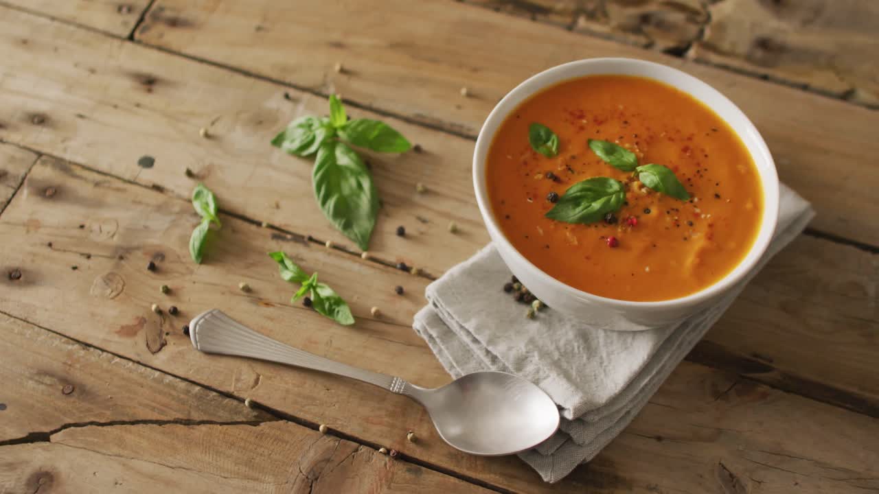 Video of cream tomato soup in bowl on wooden table with basil leaves