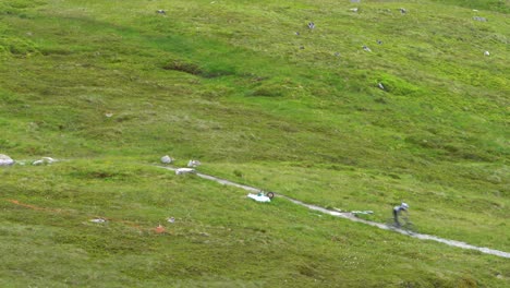 Two-mountain-bikers-descend-at-high-speed-over-the-gray-gravel-path-between-the-stones-and-the-green-lawn-of-the-highest-mountain-in-Scotland,-Ben-Nevis