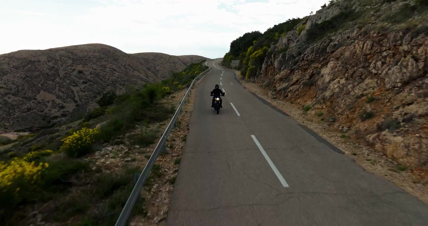 Motociclista che percorre una strada di montagna deserta, circondato da un paesaggio roccioso e dalla natura mediterranea durante un'avventura di viaggio soleggiata in Croazia.