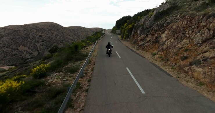 Motociclista che percorre una strada di montagna deserta, circondato da un paesaggio roccioso e dalla natura mediterranea durante un'avventura di viaggio soleggiata in Croazia.