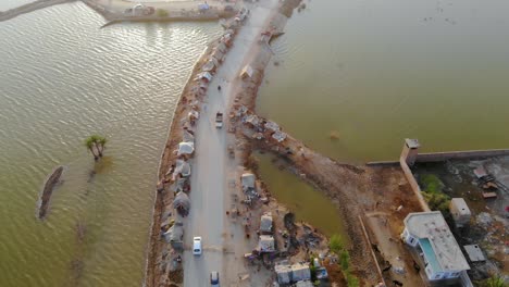 overhead aerial along view over elevated strip of land housing makeshift tents of surrounded by flooded landscape in sindh