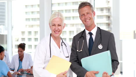 dos médicos mirando a la cámara con sus colegas detrás