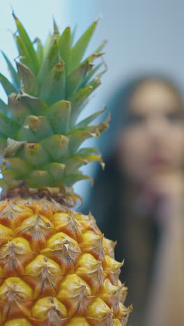 bright yellow pineapple with green top against blurred calm women sitting and eating fruits extreme close view