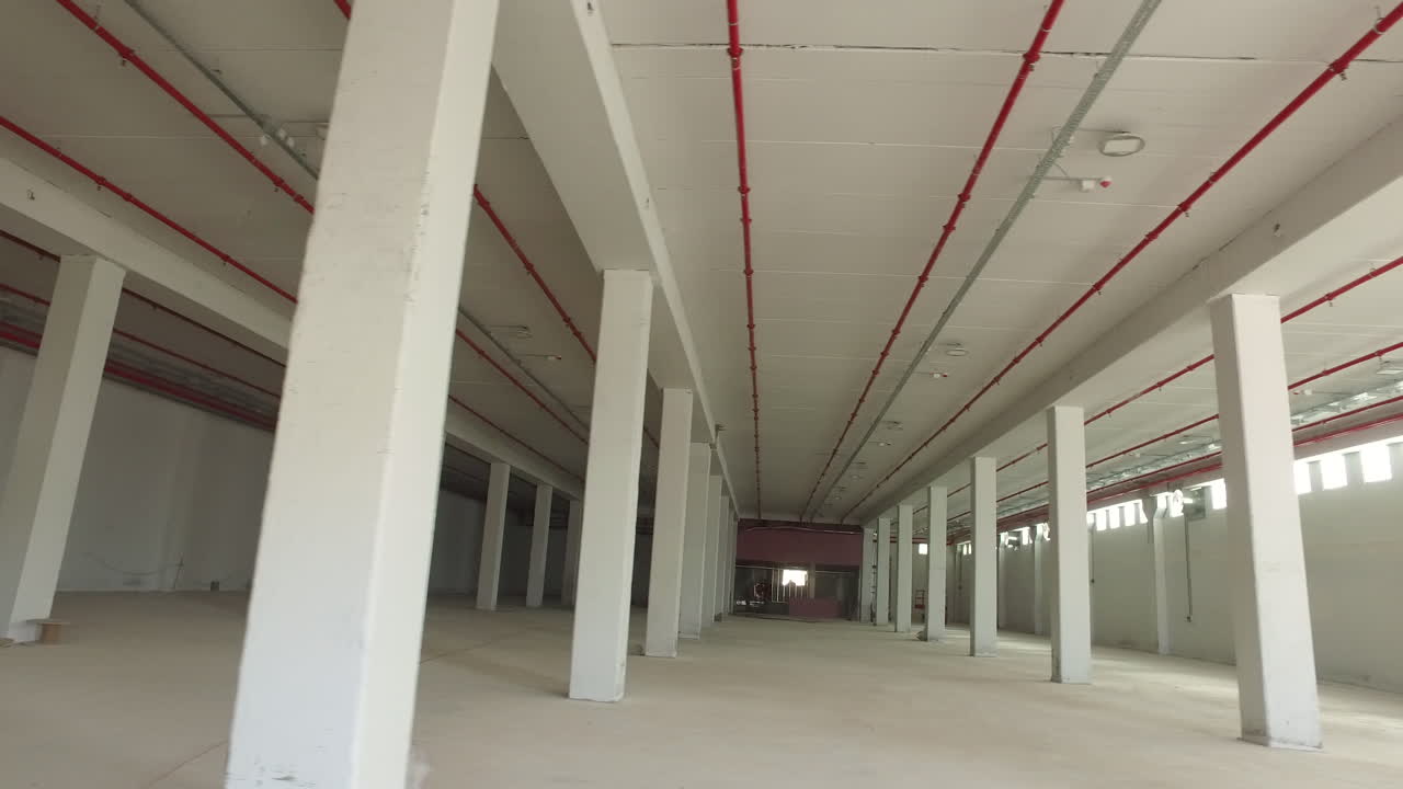 Ampi spazi con colonne bianche simmetriche e tubi rossi sul soffitto.