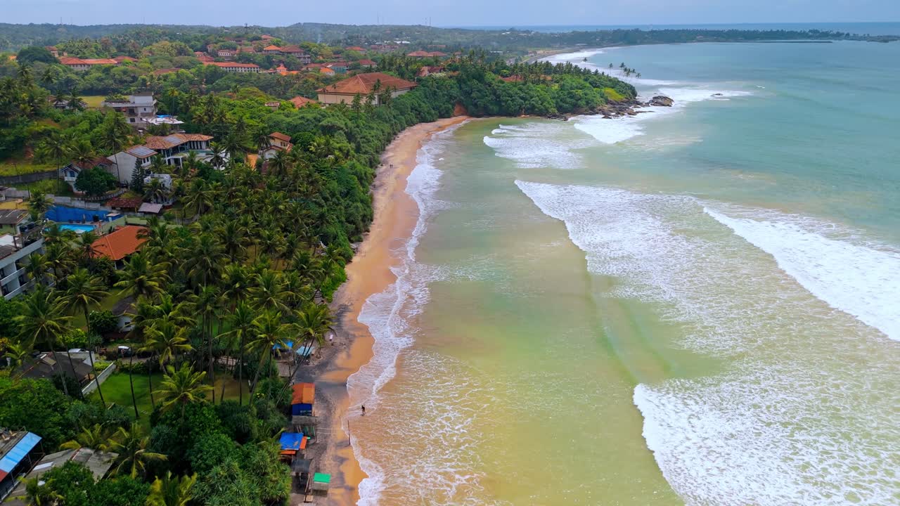 A breathtaking aerial drone shot of SK Town Surf Beach in Weligama, Sri Lanka, where lush jungle meets the ocean.