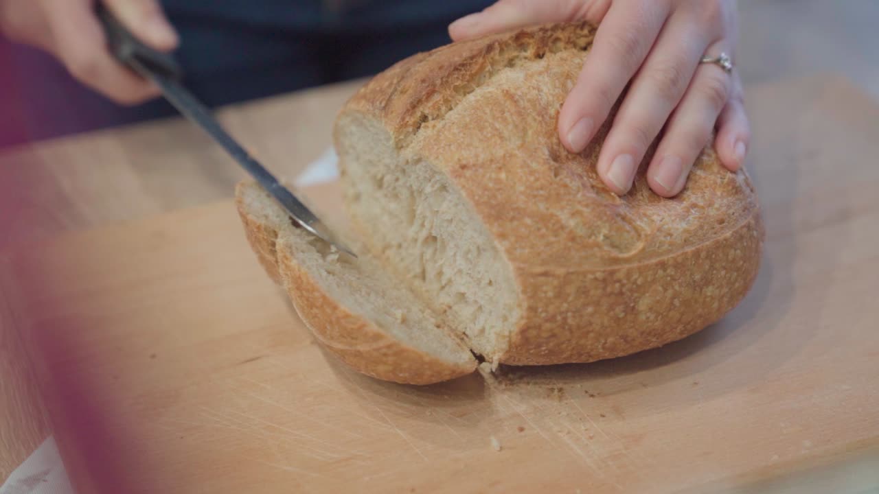 Hands cutting fresh loaf of bread, close up