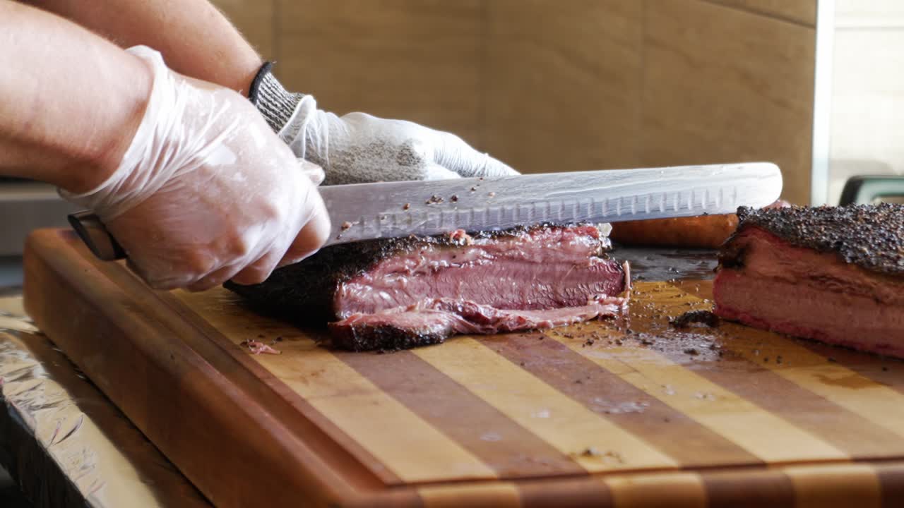 Slicer carves juicy lean Texas barbecue smoked brisket, carefeully slicing tender beef brisket for bbq plates, slow motion 4K