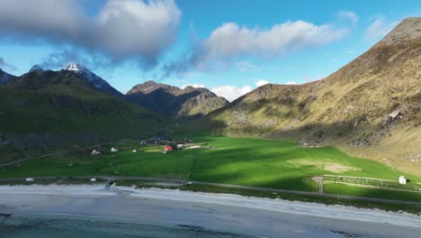 drone pulls back from haukland beach and starts revealing farmlands, ocean and mountains at sunset