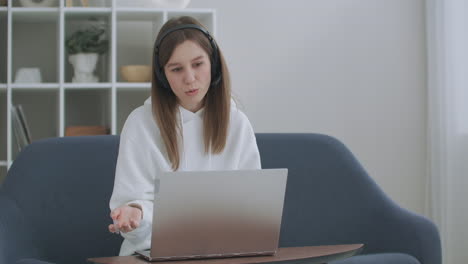 Die-Junge-Frau-Trägt-Ein-Headset-Und-Telefoniert-Auf-Dem-Laptop-Mit-Einem-Online-Lehrer,-Der-Von-Zu-Hause-Aus-Lernt.-Studentin-Macht-Sich-Beim-Lernen-Per-Computer-Webcam-Chat-Notizen.-Fernunterrichtskonzept