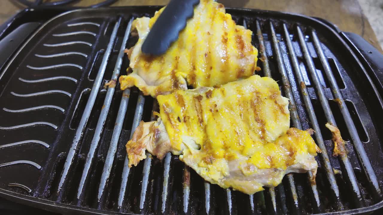 Grilled Chicken on Pan. Pieces turn with kitchen tongs on electric griddle, show grill marks