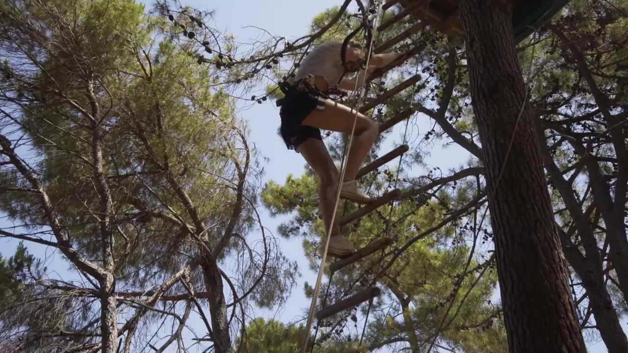 Young woman climbs down rope ladder in Rope and Tree top adventure Park