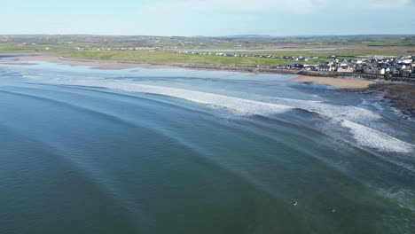 aerial tracking shot of a surfer catching a wave and standing up at lahinch beach