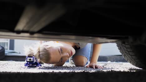 Young-adult-female-kneeling-under-car-with-adjustable-scissor-jack-checking-positioning