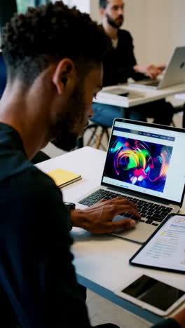 people working on laptops and tablets in a bright, modern coworking office, including individuals focused on digital design and data