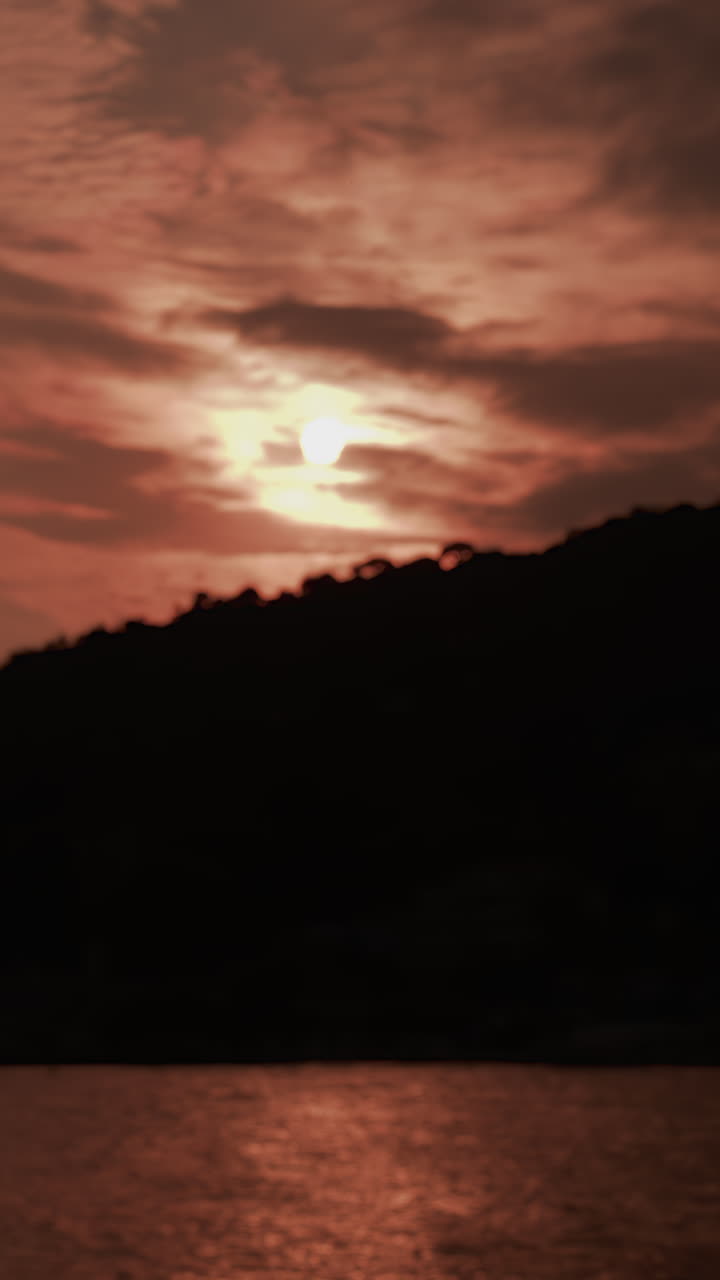 A dramatic sunset view showing a dark cliff silhouette with golden sunlight shimmering across the sea. Vertical