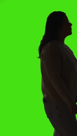 Vertical-Video-Silhouette-Shot-Of-Young-Woman-Walking-Slowly-Across-Frame-Against-Green-Screen