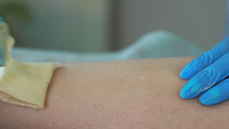 un primer plano de la mano en guantes de goma se aplica a la pasta de depilación y por tecnología especial shugaring elimina el pelo