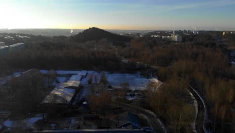 Toma-Aérea-De-Un-Edificio-Industrial-Rodeado-Por-Un-Parque-Forestal-Durante-El-Invierno-Al-Amanecer