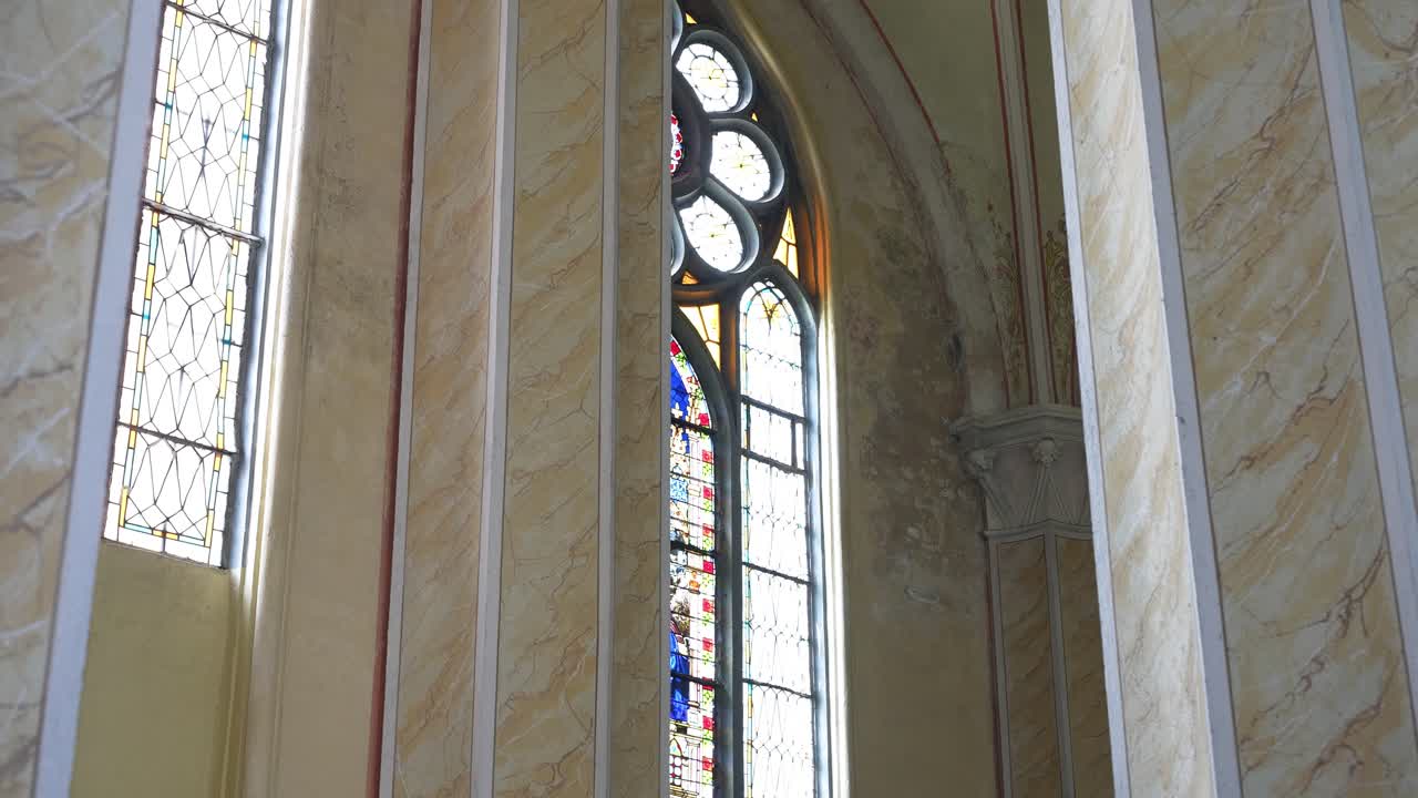 Ammira le intricate vetrate colorate nella Chiesa di San Francesco d'Assisi di Šilalė. La luce filtra attraverso le vivaci finestre, proiettando motivi colorati in un'atmosfera serena e sacra. Nessuna persona visibile