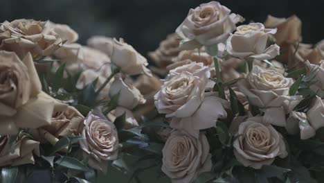 close-up of withered white roses in full bloom, arranged in a bouquet with green leaves. the petals curl slightly, creating a vintage, nostalgic aesthetic. dark, blurred background enhances contrast.