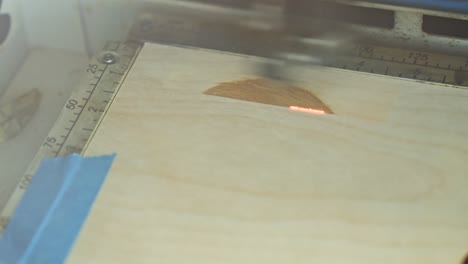 un grabador láser grabando rápidamente un diseño en madera en una mesa de trabajo