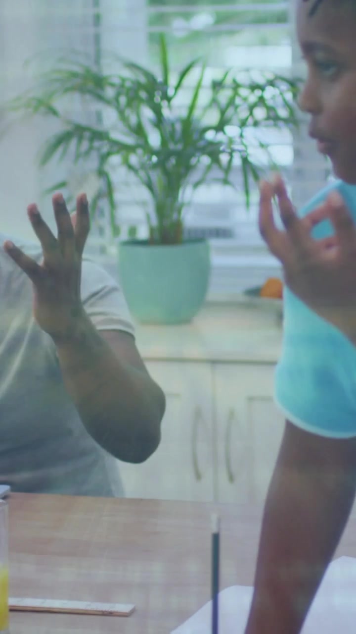 Vertical video: Child raising hand initiating dad helping study in kitchen, question mark popping
