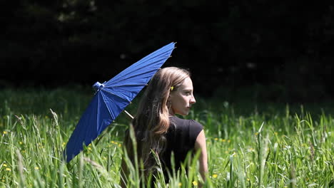 a woman sits in a grassy field holding a blue umbrella