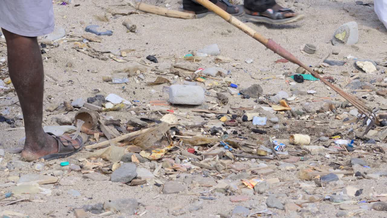 man collecting waste plastic with rake agriculture tool in Carter road beach mumbai india closeup shot