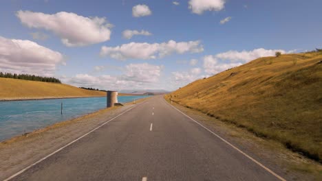 Sunny-drive-along-road-next-to-artificial-power-canal-in-Canterbury,-New-Zealand