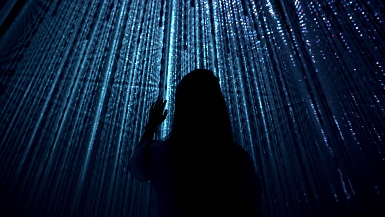 A cinematic shot of a girl interacting with the illuminated blue lights art installation at TeamLab Planets in Tokyo.